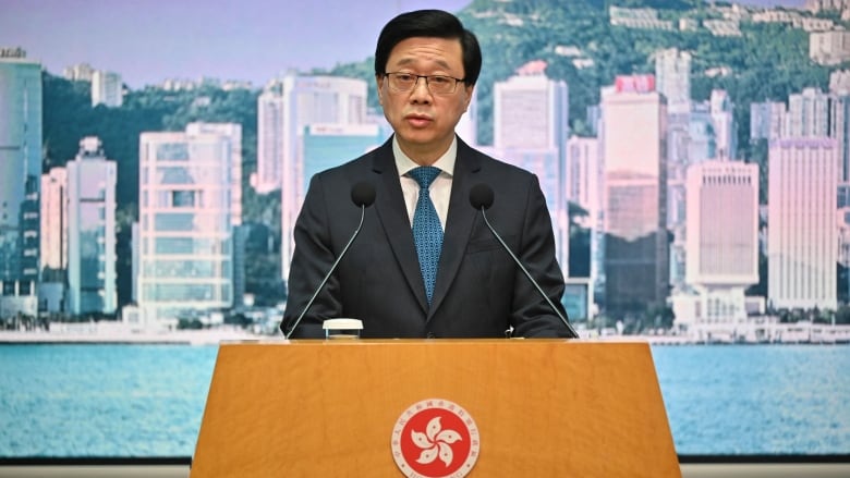 A bespectacled Asian man in a suit speaks at a podium.