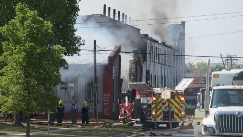 Firefighters stand next to an industrial building that's on fire.