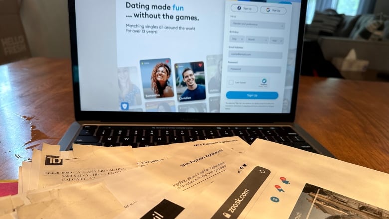 A lap top sits open on a dining table. The screen shows photos of two people. There are papers on the table.