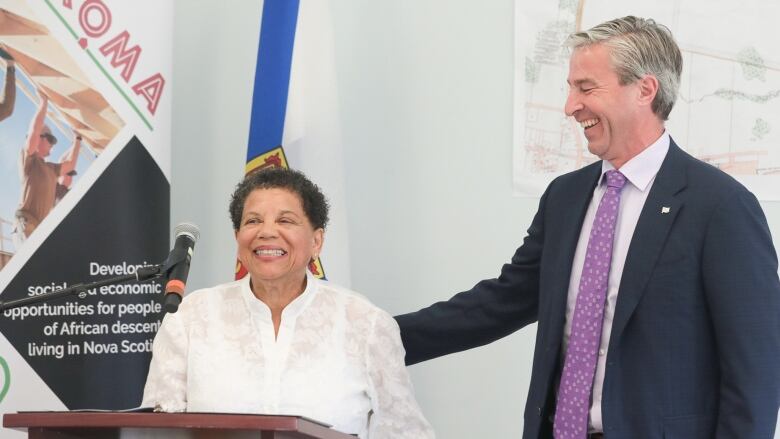 A woman wearing a white blouse stands behind a podium next to a man wearing a suit and tie.