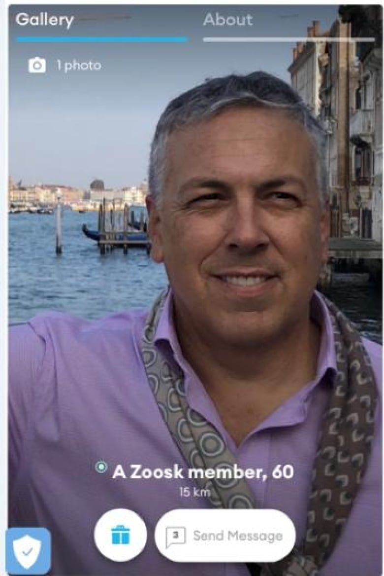 A picture of a man in his 50s wearing a purple collared shirt standing in front of a bay of water in Italy.