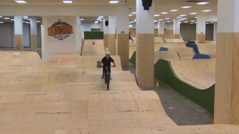 An indoor bike park with varied terrain is pictured, one person is biking. 