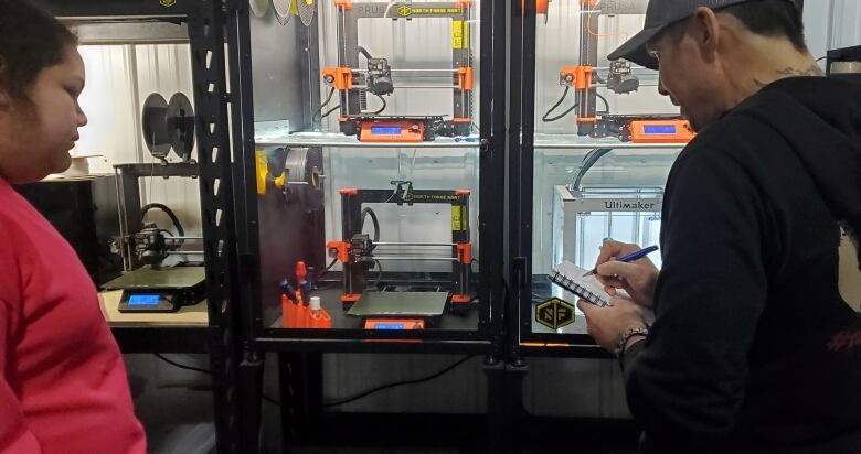 A young girl standing in front of a 3D printer with one of the workers from North Forge North. 