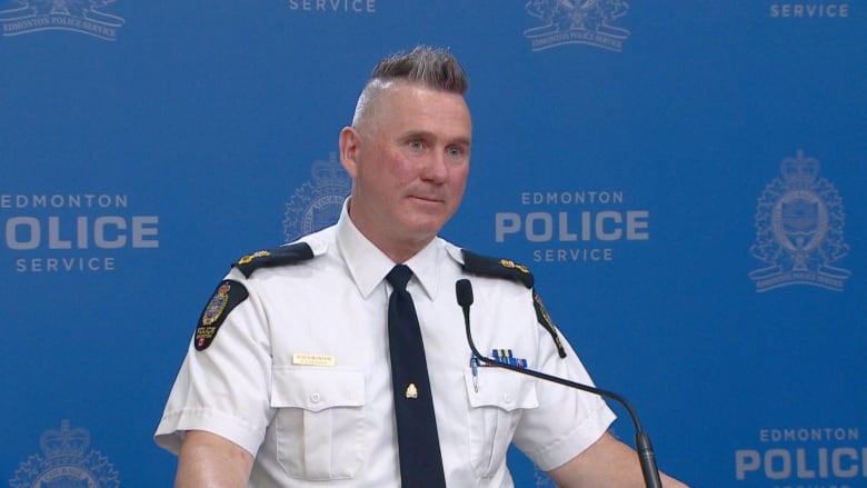 Police officer speaks into a microphone in front of reporters.