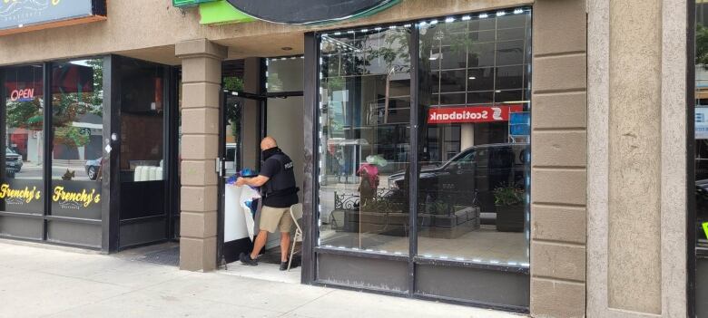 A police officer removing signage from a store front.