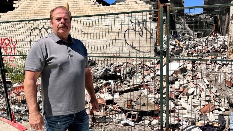 A man stands in front of a building that has been partially destroyed. 