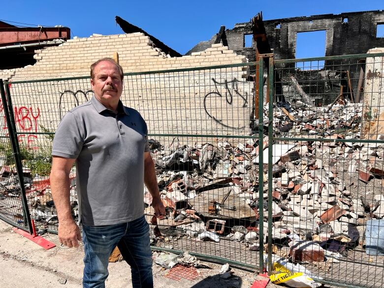 A man stands in front of a building that has been partially destroyed. 