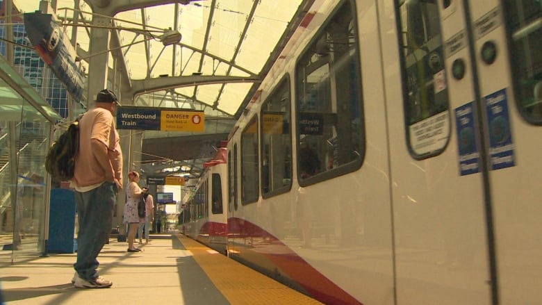 A passenger stands on an LRT platform as a Ctrain rolls through. 