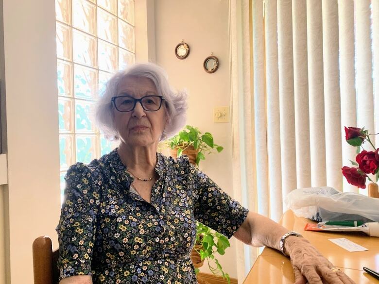 A woman in a floral dress sits at a kitchen table. 