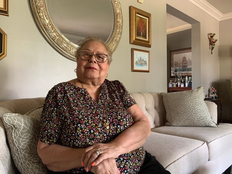 A woman in a floral shirt sits on a couch. 