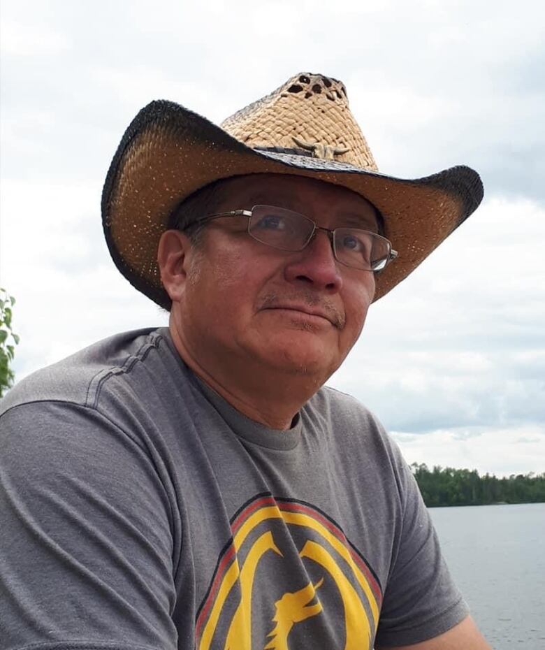 A man wearing a straw hat with a lake and forest in the background.