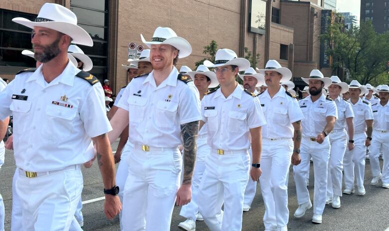 men dressed in white uniforms march in unison along a Calgary street.