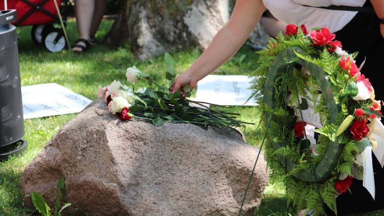 A woman lays a rose on a memorial stone. 