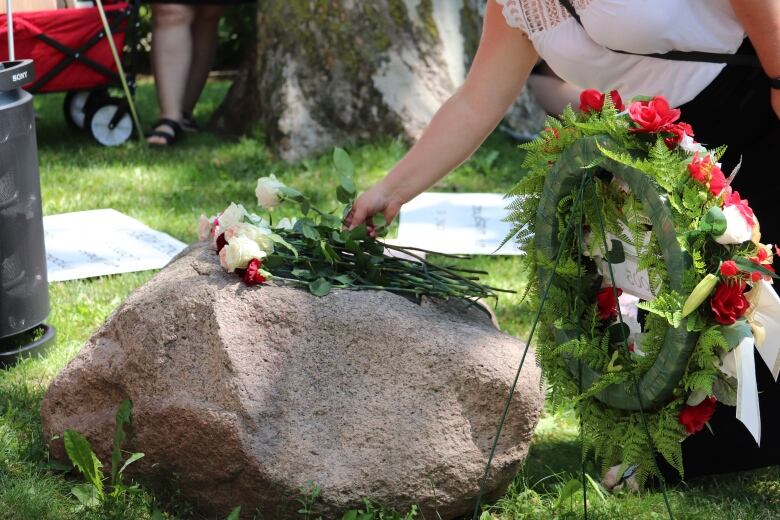 A woman lays a rose on a memorial stone. 