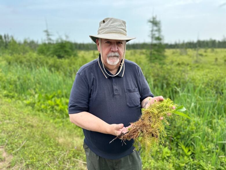 A man in a Tilly hat stands next to a bog 