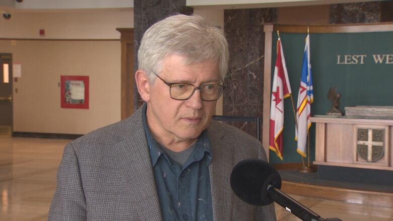 A man wearing a suit stands in front of a microphone at Confederation Building.