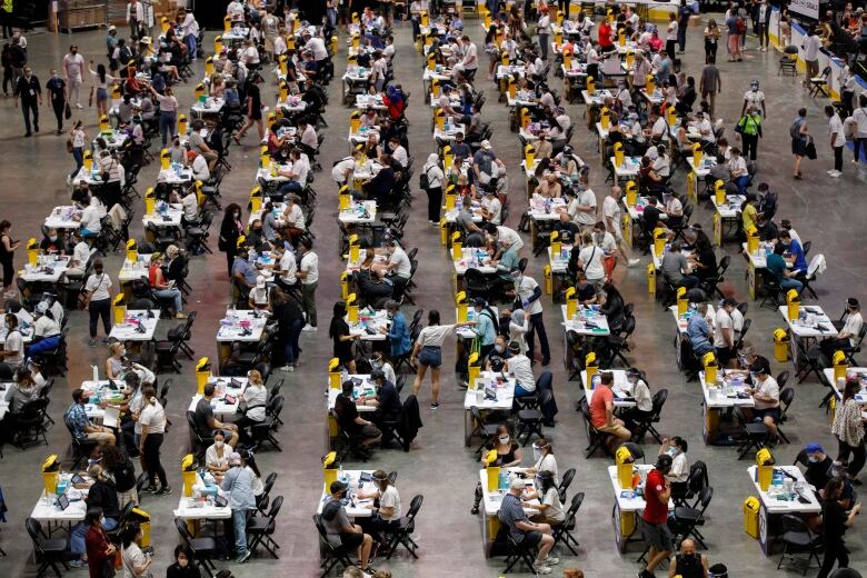 People sit at tables in an arena waiting to be vaccinated.