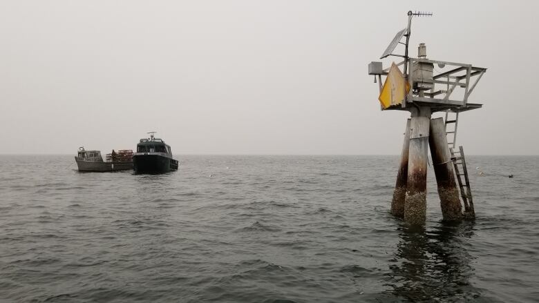 Two boats are tied together on the water with smoky skies in the background and a water marker in the foreground