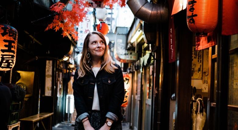 A woman in jean jacket walking down street lined with lit up lanterns.