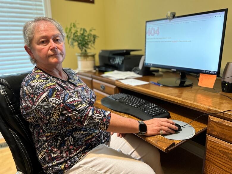 A woman sits at a computer with her hand on the mouse.