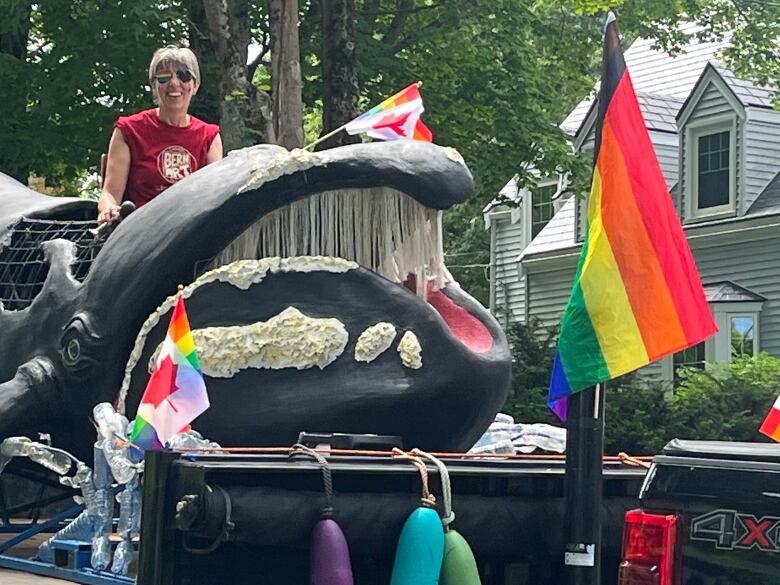 A person sits on a float with a large figure of a whale and pride flags.