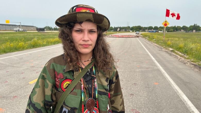 A woman stands on a road with an upside down Canadian flag in the background.