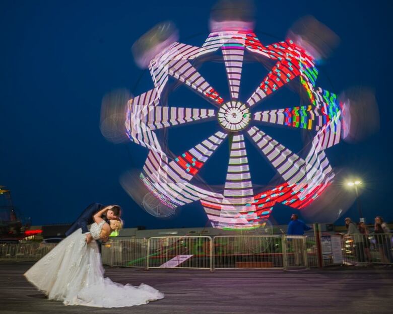 A groom and bride kiss in front of a Ferris wheel. 