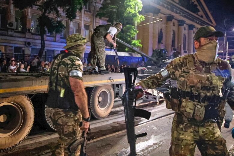 Three mercenaries hold weapons as one of them stands on a truck.