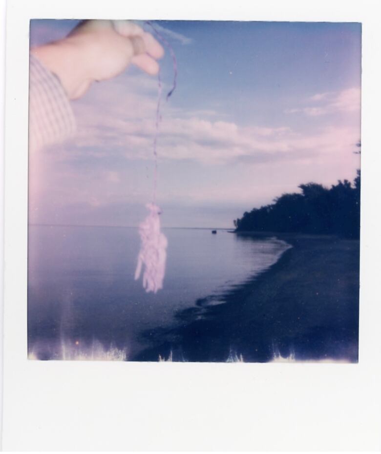 A man's extended hand, holding up a string with balloon remnants attached. The lake shoreline is in the distance. 