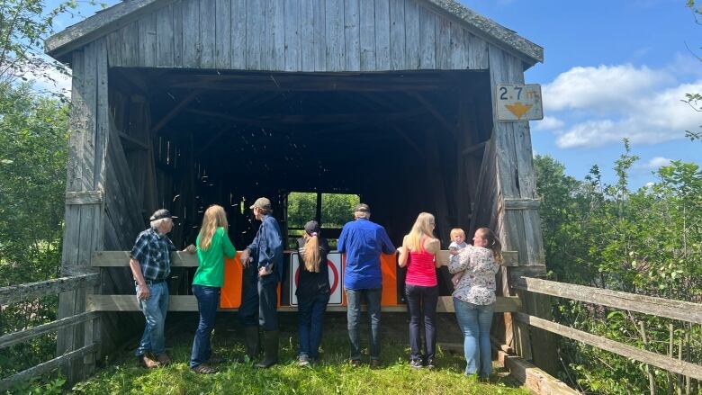 Eight people have their backs to the camera as they look into a covered bridge, learning on a barricade over the front.