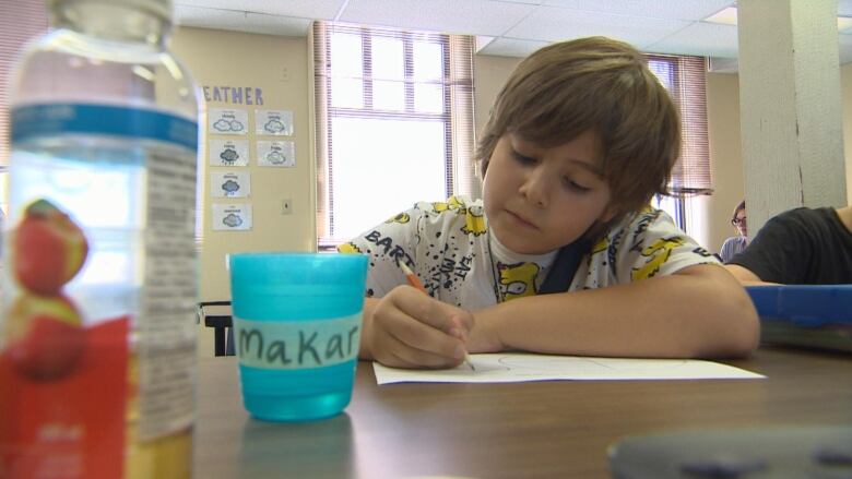 A young boy writing in a notebook with a pencil.