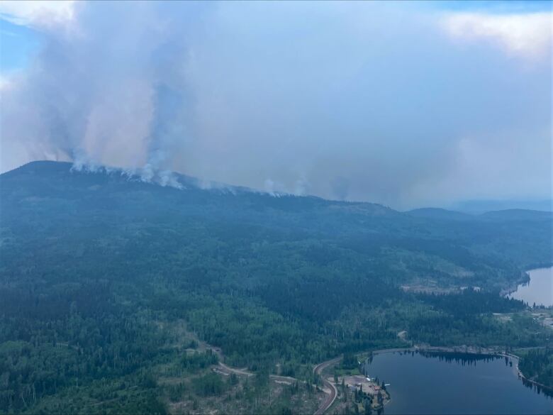 Smoke rises from a hilltop in the background of a scenic lake.