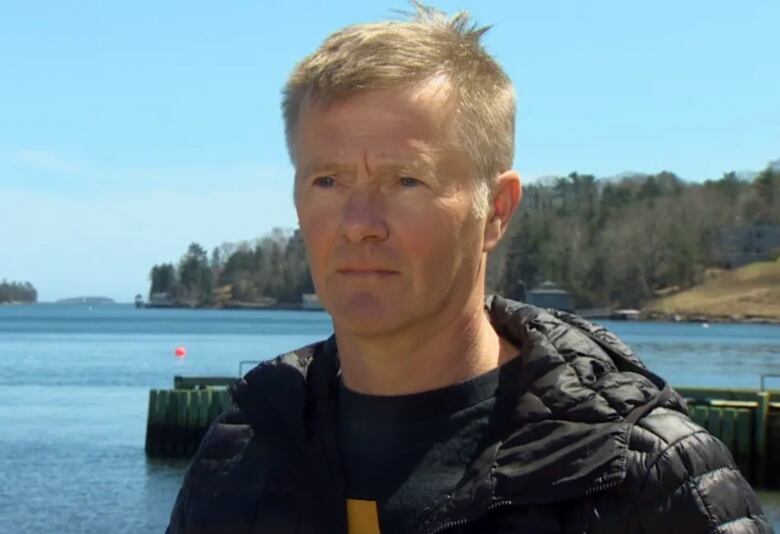 A man wearing a black jacket standing near the ocean. 