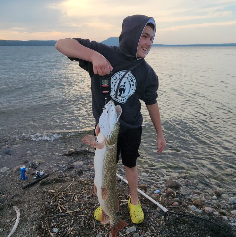 A young man holds a fish he caught. 