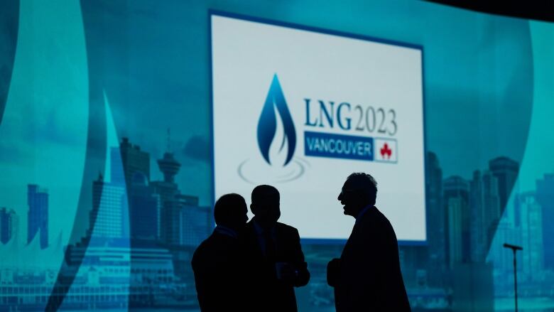 Several men are silhouetted in front of a wall with a projected sign reading 'LNG 2023 Vancouver.'