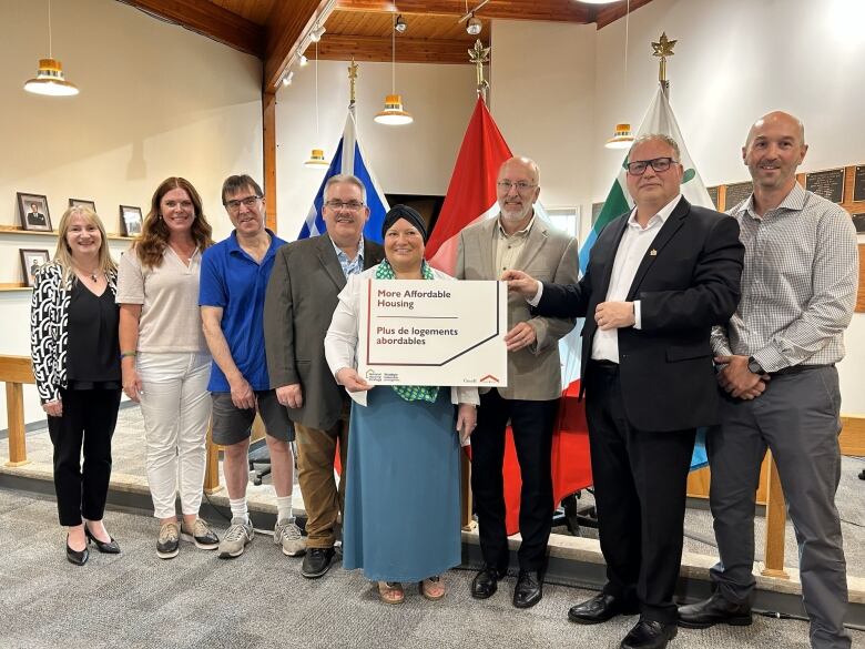 Eight people stand side by side smiling. The woman in the centre is holding a sign that reads 'More affordable housing.'