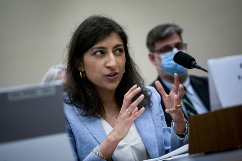 A woman in a blue blazer gestures while speaking into a microphone. 