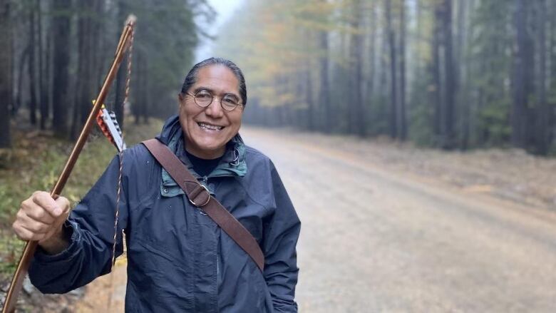 An Indigenous man stands with a bow wearing a blue jacket