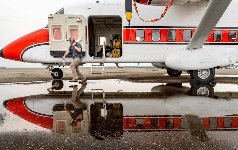 A man is pictured holding a cell phone while walking near an aircraft.