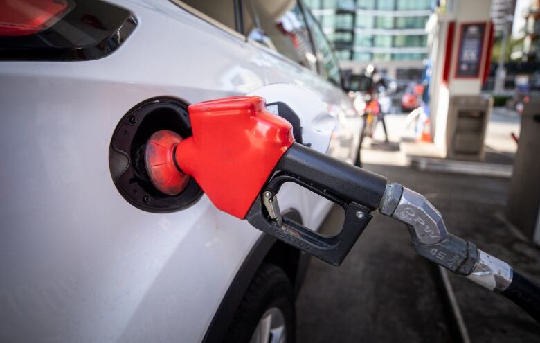 A red gas pump is lodged in a white car's gas tank.