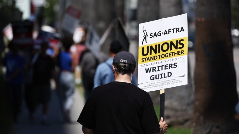 A person facing away from the camera holds a sign that reads, 'Unions Stand Together.'