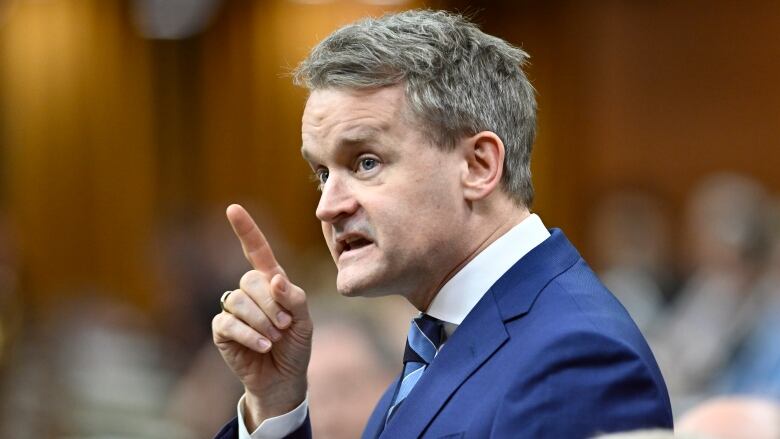 A white man points his finger while standing among a group of people.