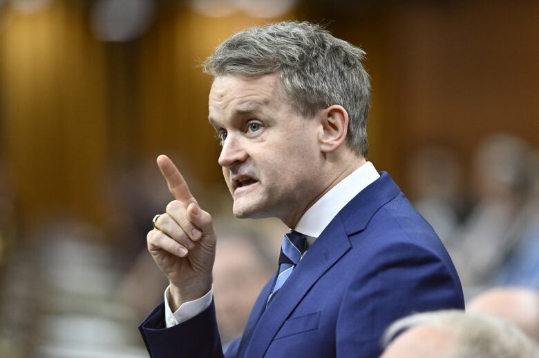 A white man points his finger while standing among a group of people.