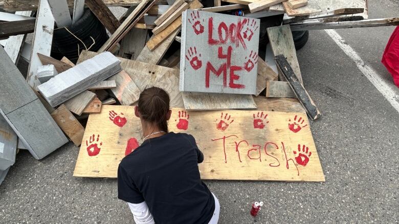 A woman paints a protest sign near a blockade made of pieces of wood. 