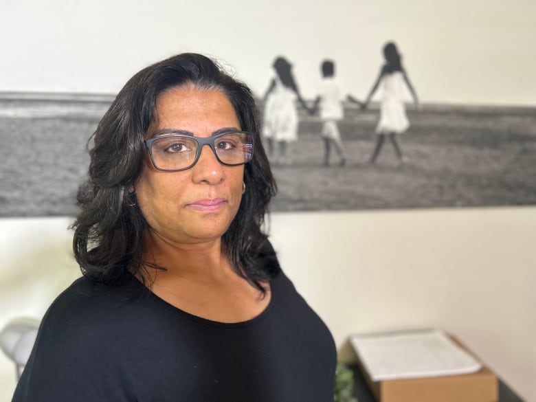 A woman stands in front of a black and white photo with three women in it.