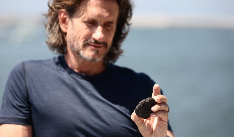 A man with a beard holds a black rock.