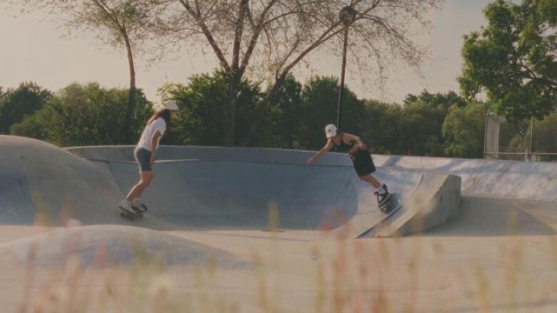 Two skateboarders ride in a bowl at a skateboard park. 