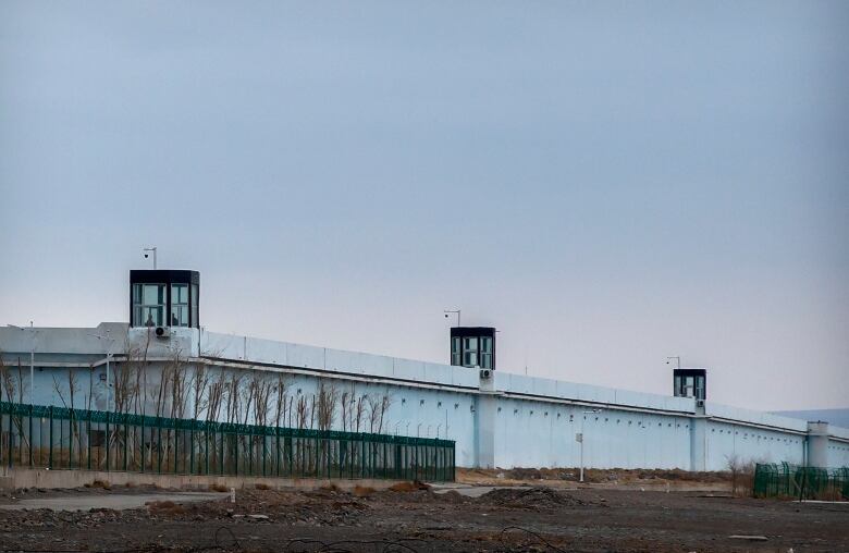 People stand in one of three glass towers atop a long, low cement building surrounded by green fencing.  