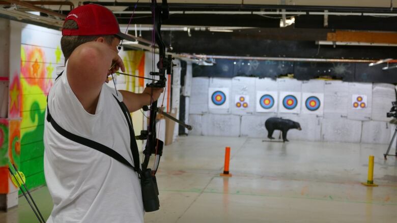 A young metis boy points his bow and arrow towards a 3D bear target at an indoor shooting range in winnipeg