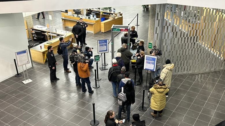 People are lined up in front of a walk-through metal detector inside a large lobby of a building.